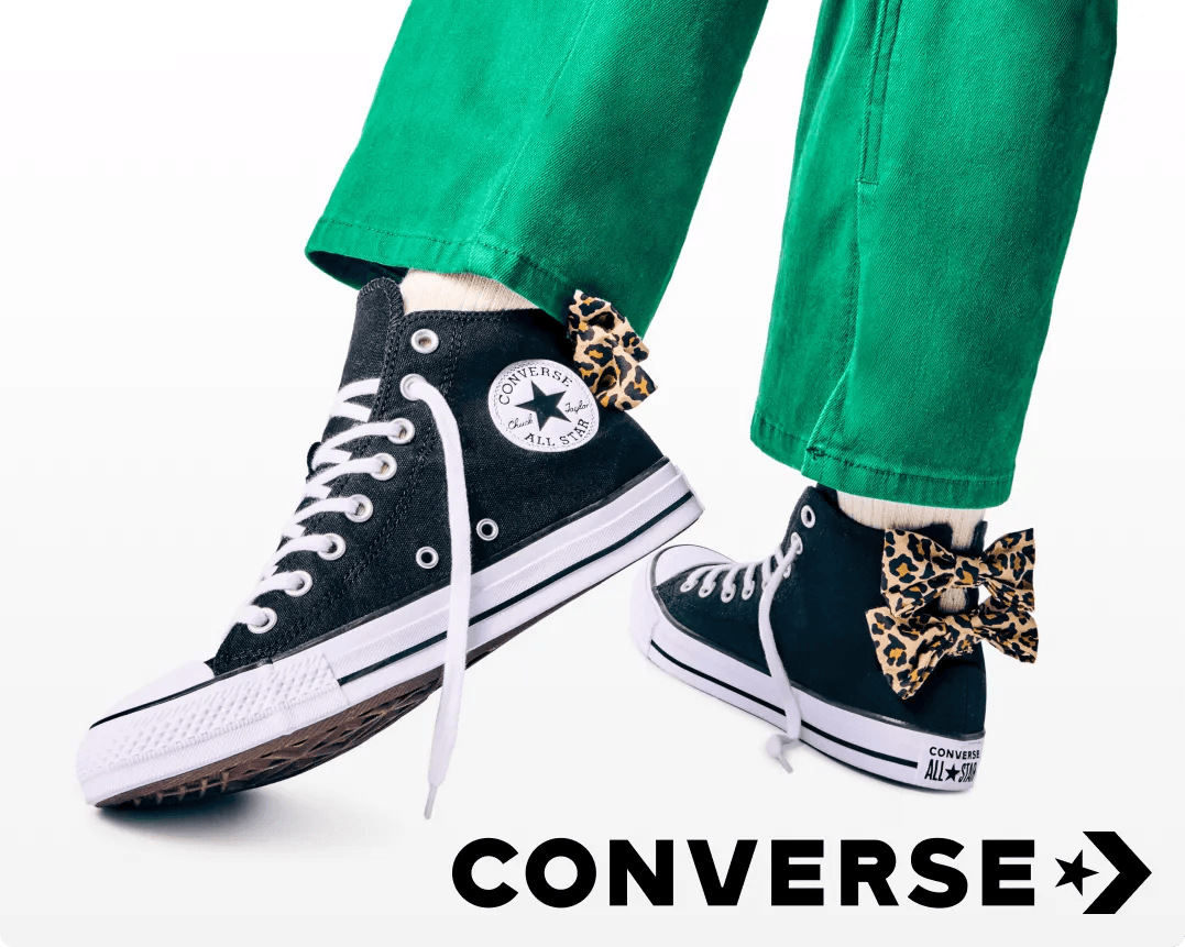 Featuring a girl's legs with green pants and black Converse with Cheetah print bows on the back.