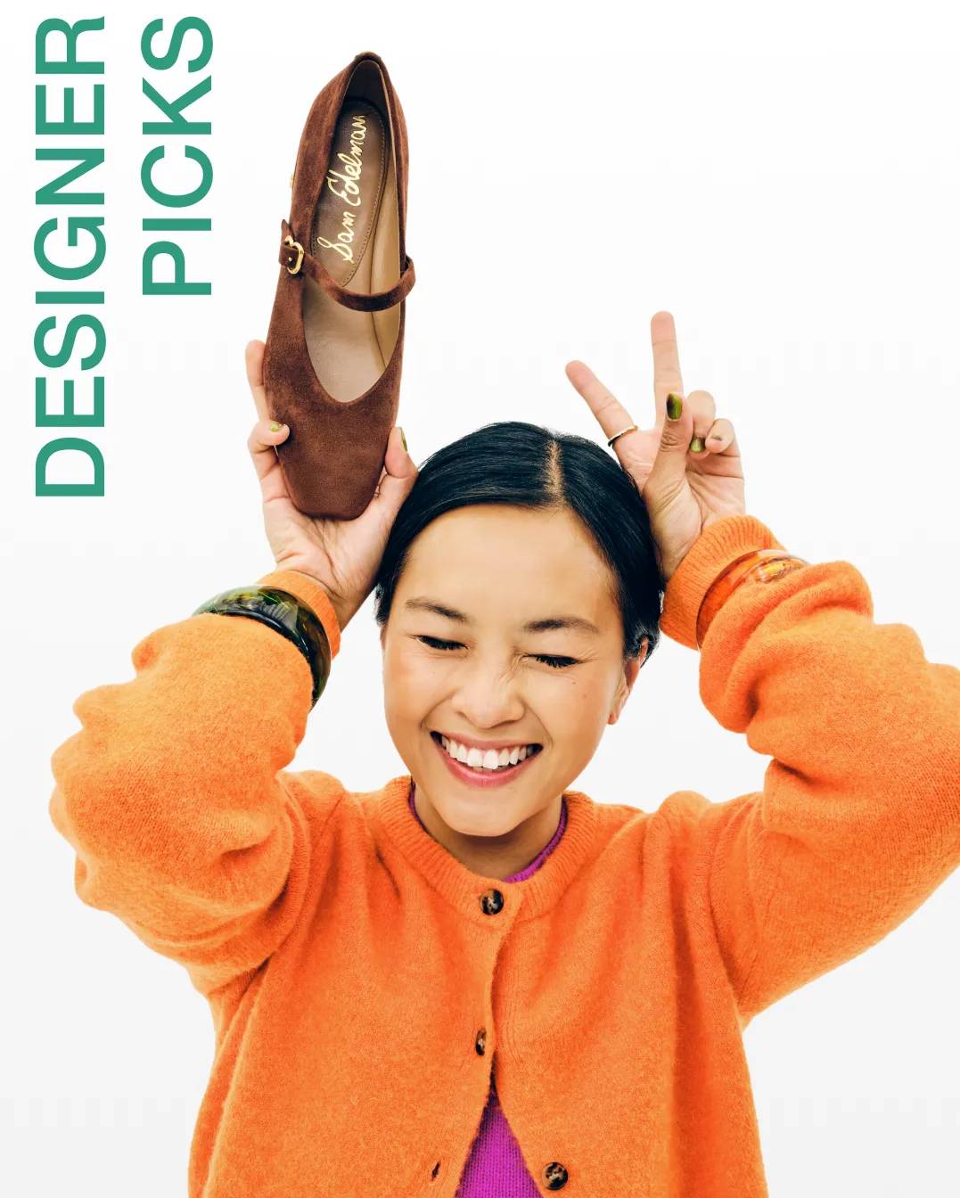 Featuring a woman wearing a bright orange sweater holding a brown suede Mary Jane flat.