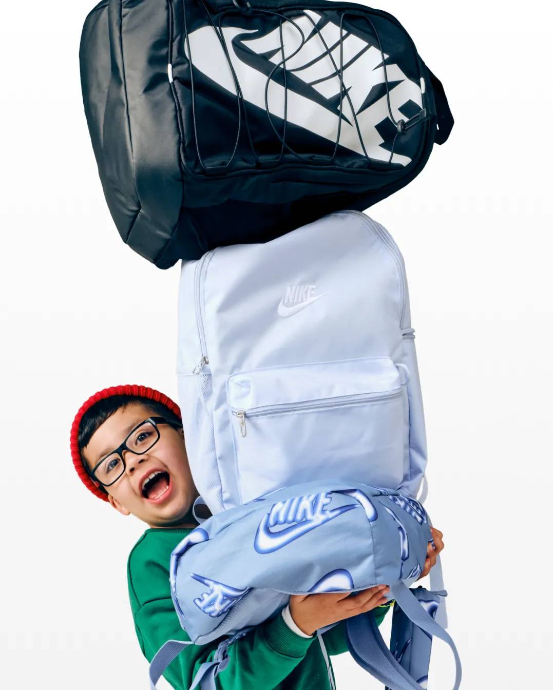 Featuring a child holding a stack of backpacks.