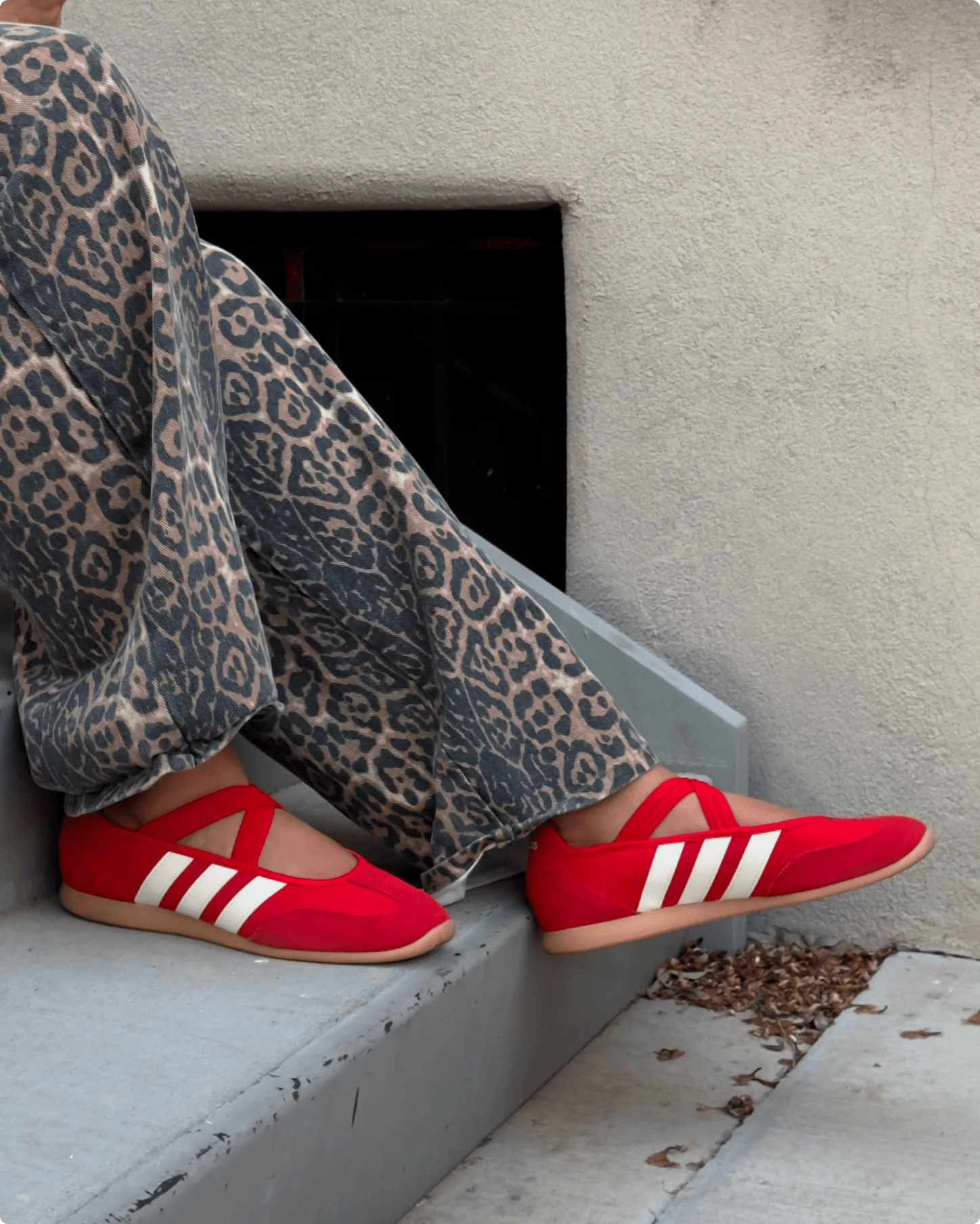 Featuring a model's legs with animal print pants and bright red Adidas Barreda Mary Jane sneakers.