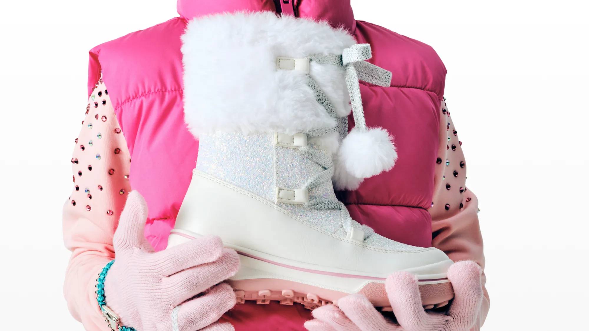 Women holding a pair of white and pink furry snow boots.