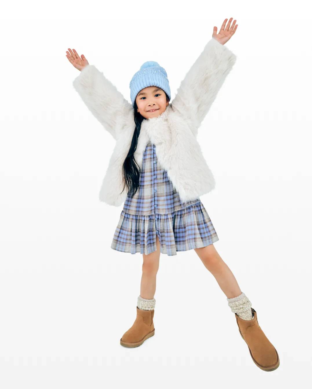Featuring a child wearing winter boots, a hat and furry jacket.
