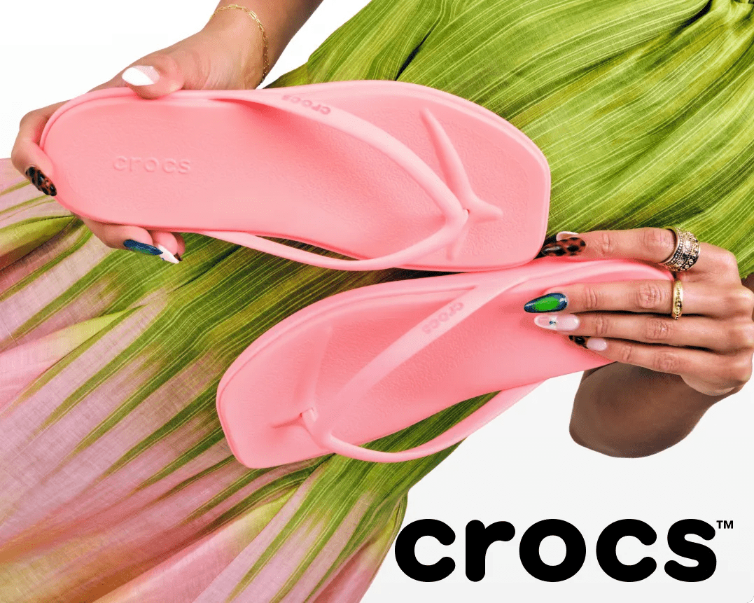 Featuring a woman holding a pink pair of Crocs flip flops.