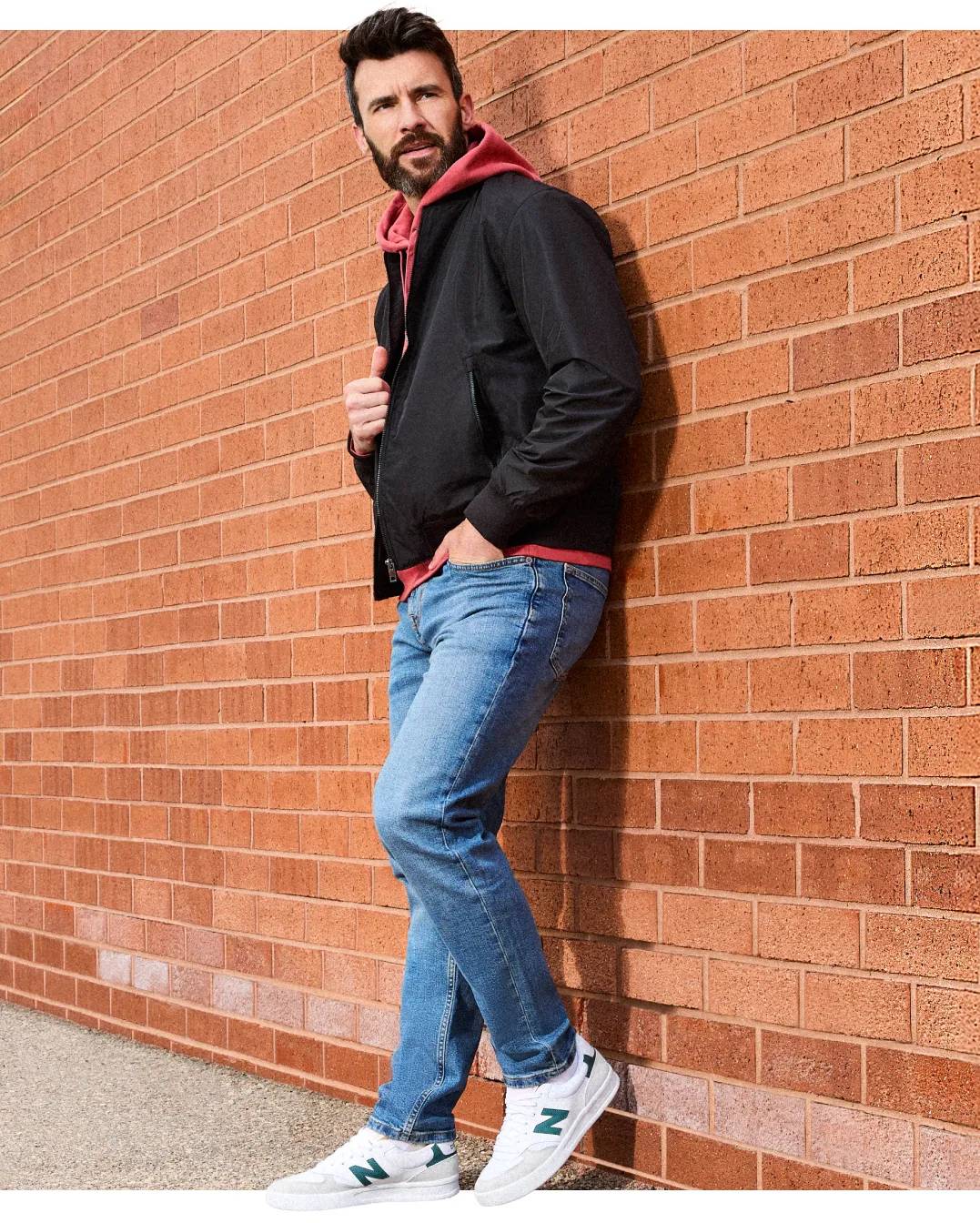 Man leaning against brick wall wearing white New Balance sneakers