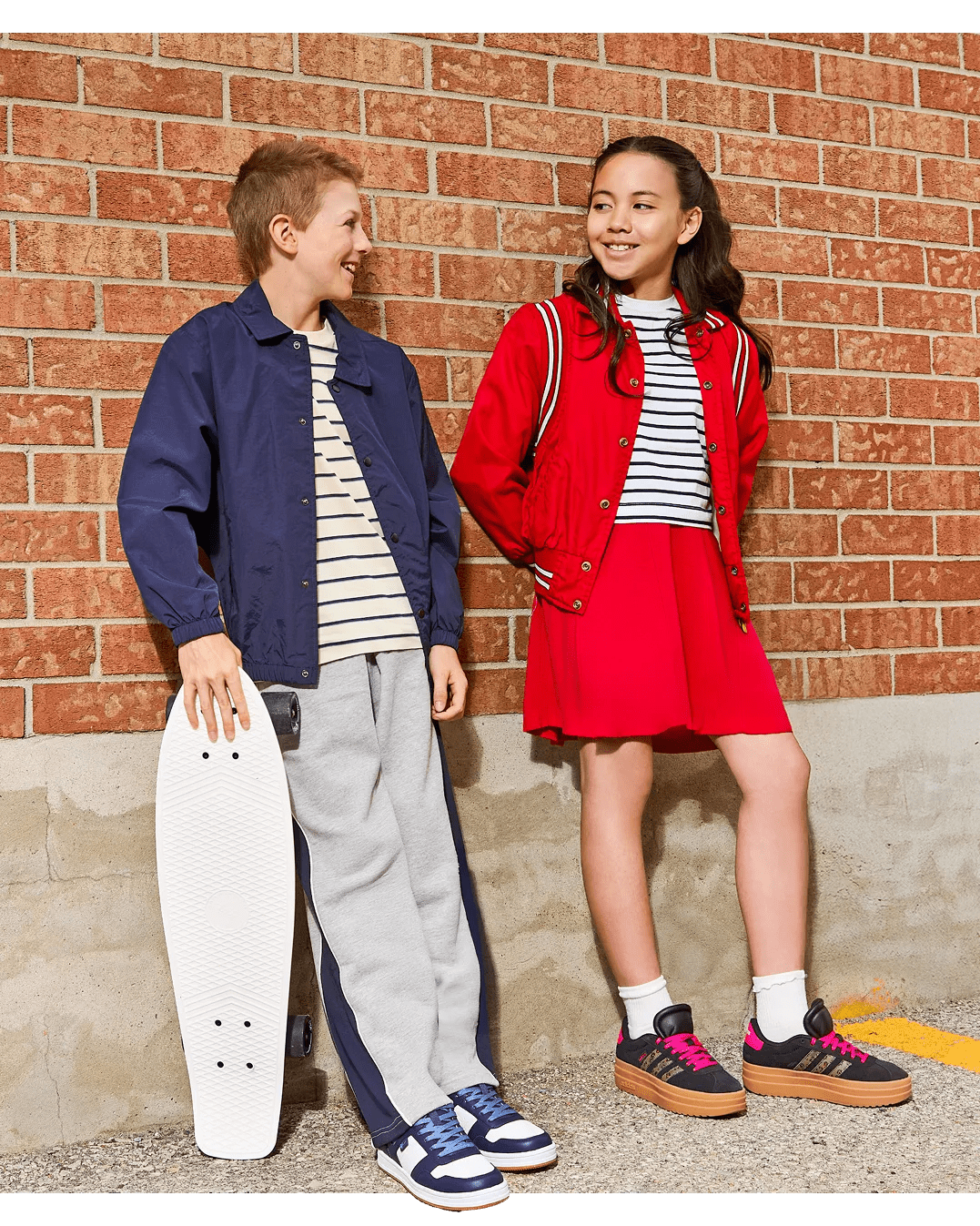 Boy and girl leaning against brick wall wearing skate shoes