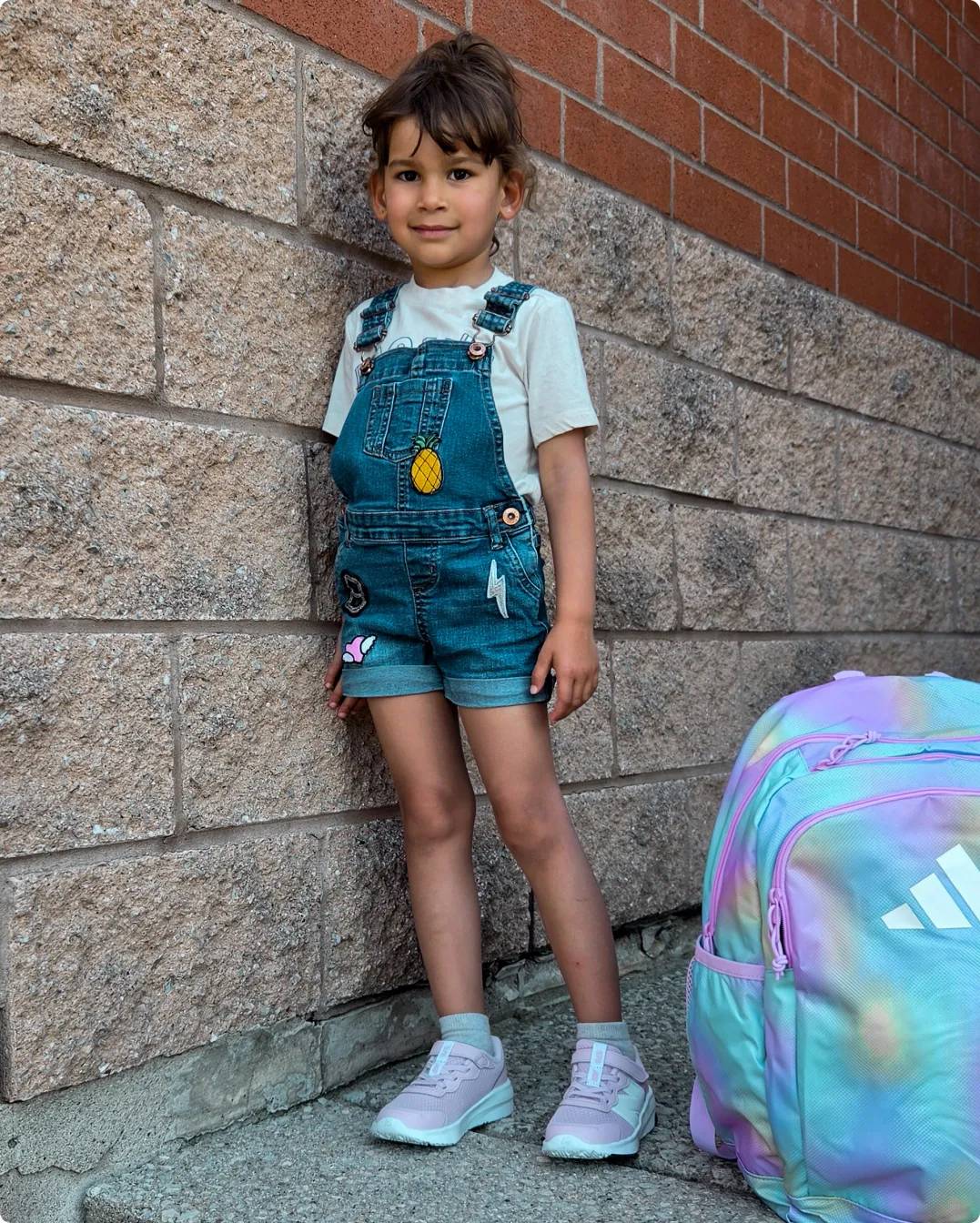 Girl leaning against brick wall with backpack on the ground