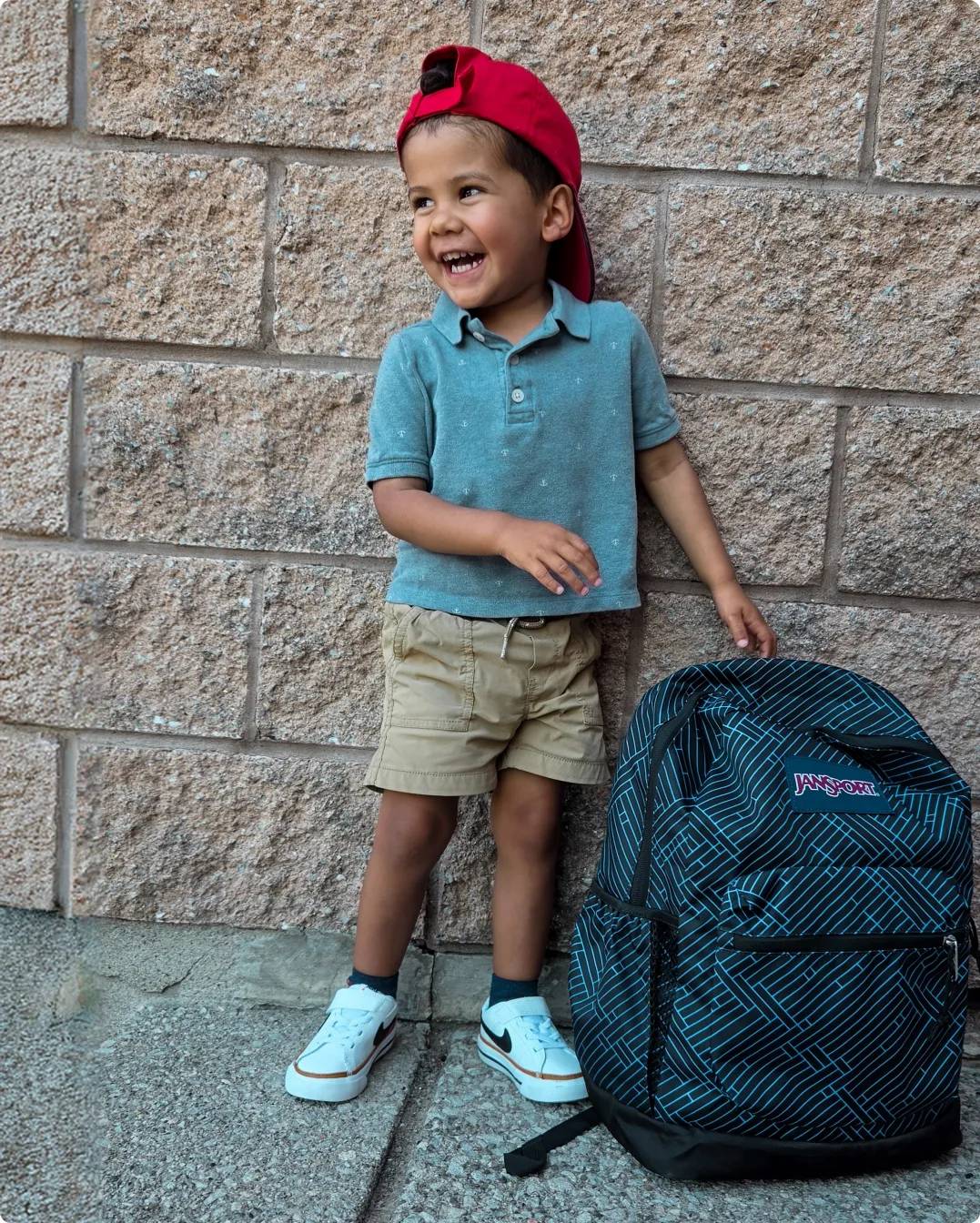 Boy with backwards red cap laughing with his backpack
