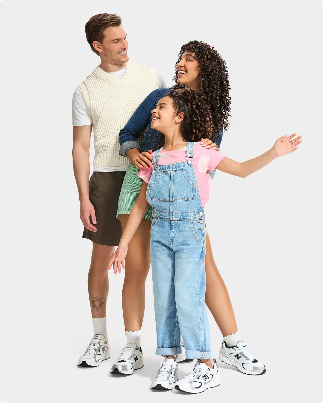 A girl wearing overalls and a woman in green shorts, a man in a yellow sweater vest