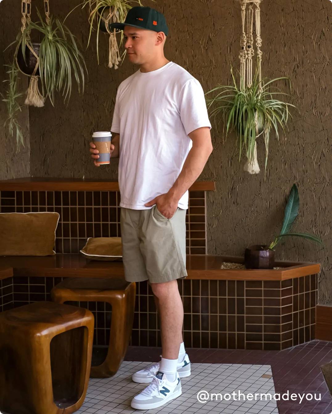 Man wearing white New Balance sneakers while holding a coffee
